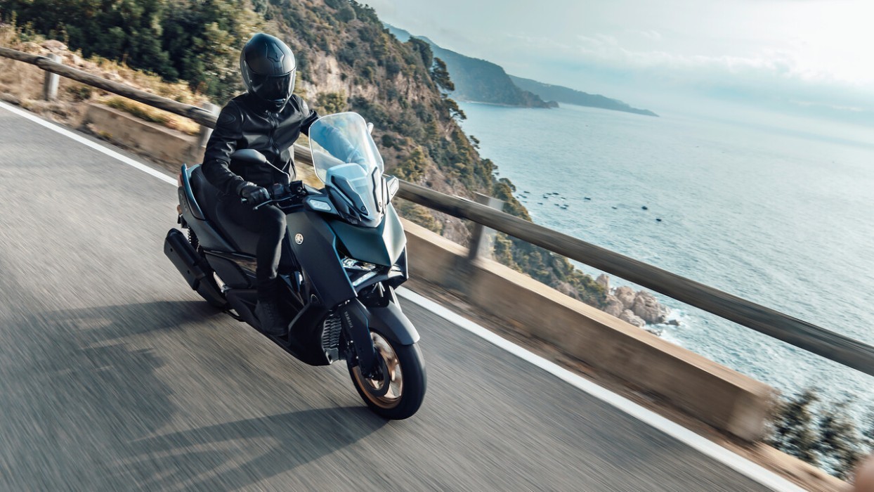 Action image of Yamaha XMAX 300 scooter in petrol green colourway, riding down mountain road by the ocean