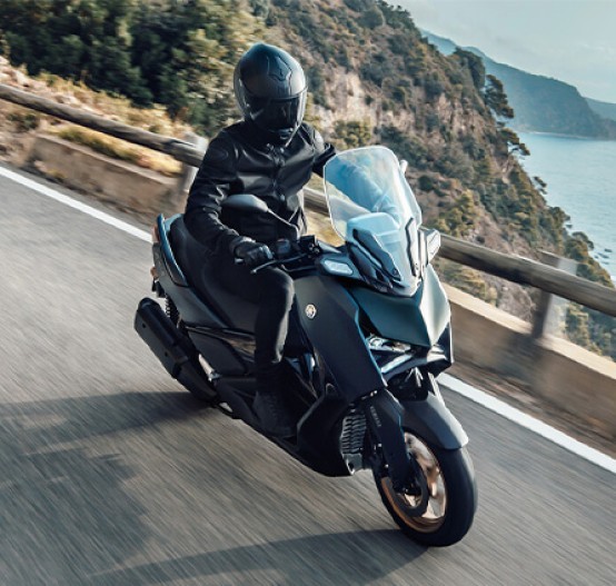 Action image of Yamaha XMAX 300 scooter in petrol green colourway, riding down mountain road by the ocean