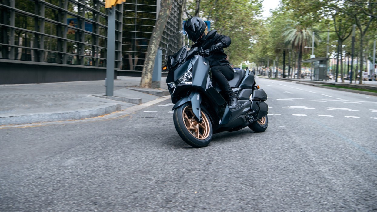 Action image of Yamaha XMAX 300 scooter in petrol green colourway, riding through city intersection