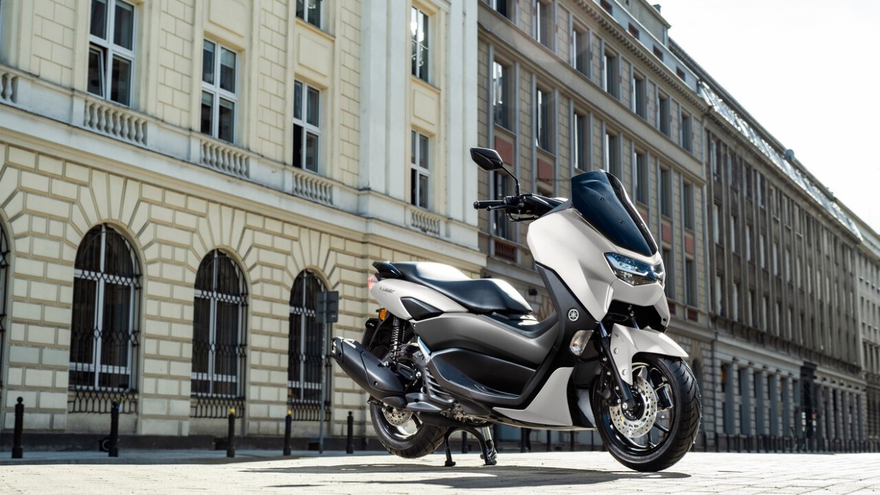 Static image of Yamaha NMAX 155 scooter in white colourway, parked on city street
