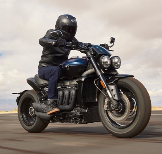 Rider on a 2024 Triumph Rocket 3 R Storm Cruiser motorcycle in motion, featuring a sleek black and blue design, at Brisan Motorcycles Newcastle