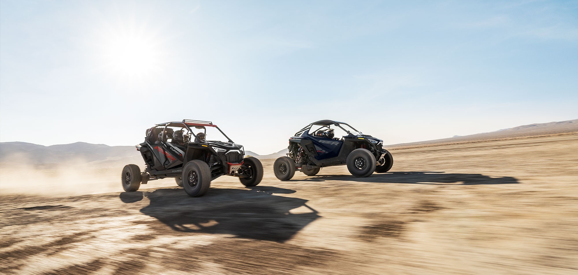 Action image of two Polaris RZR off-road vehicles going fast on a flat, dry desert