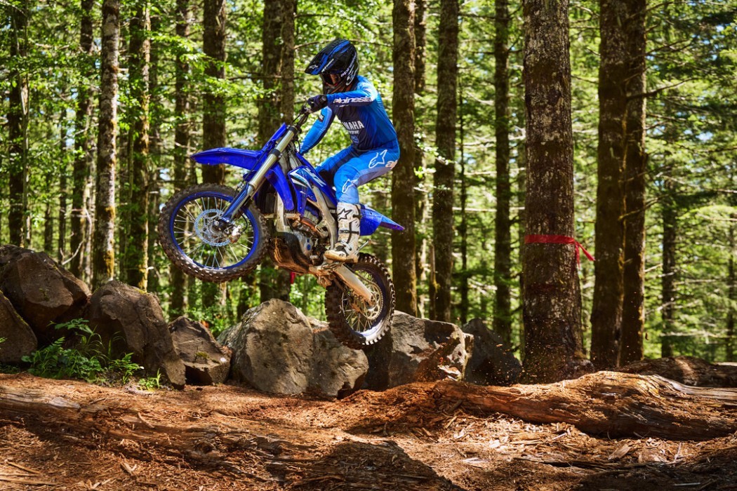 YZ450FX 2025 static image of enduro bike doing jump in forest