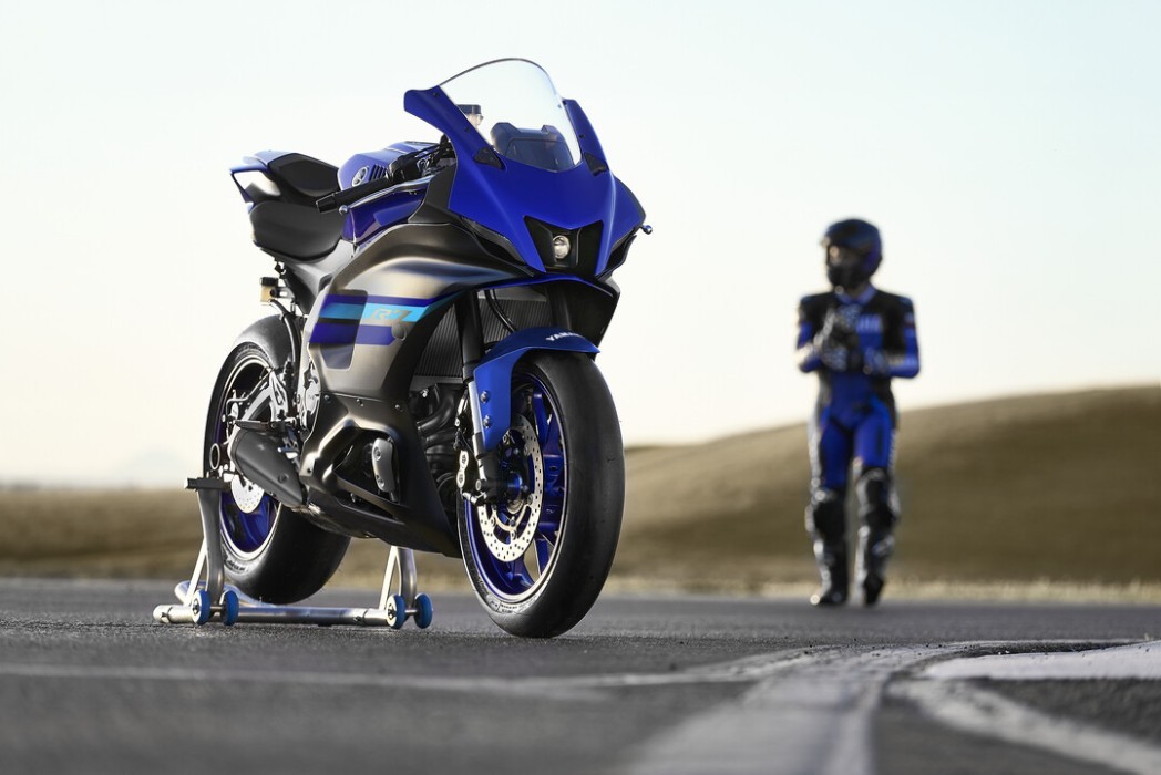 Outdoor static image of Yamaha YZF-R7 LAMS 2024 in Blue Colourway, front three quarter with rider in background approaching bike
