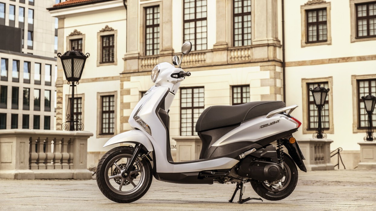 Static image of Yamaha D'elight 125 scooter in pearl white colourway, side on in city square landscape